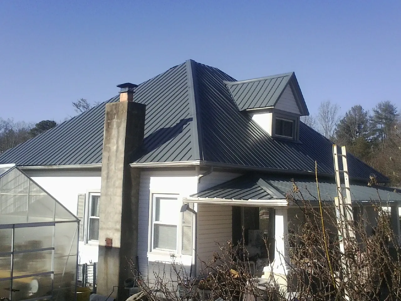 Dark blue standing seam metal roof on a white farmhouse with dormer — Slate & Tile Roof Repair by Roofing Brothers in Big Bend