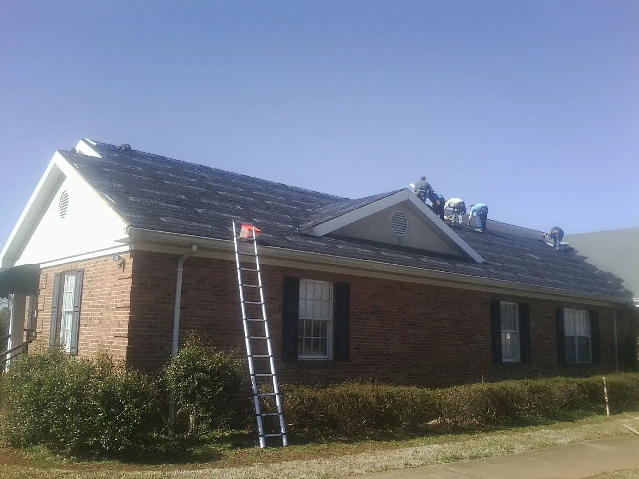 Crew tearing shingles off a brick ranch roof with a ladder set — Emergency Roof Repair work by our crew in Big Bend