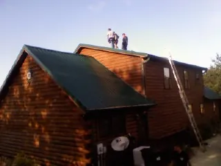 Crew on the ridge of a green metal roof on a two story log home in Big Bend
