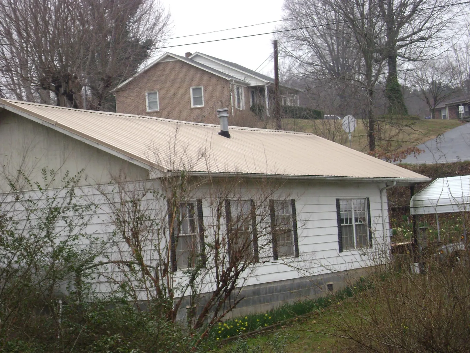 Tan metal roof on a white sided house set into a hillside — Commercial Roofing by Roofing Brothers in Big Bend